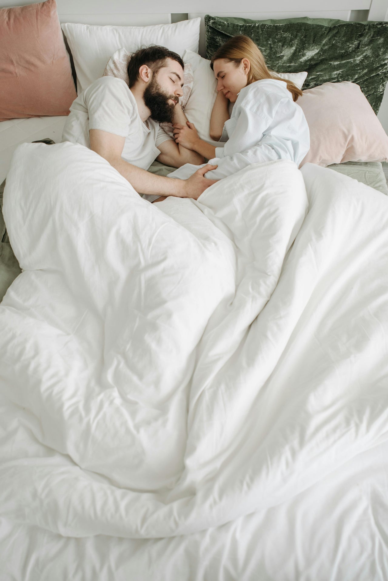 Couple cuddling in bed with white bedding and assorted pillows for cozy bedroom decor