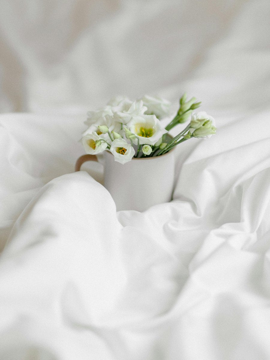 White lisianthus flowers in a beige ceramic cup on soft white fabric background