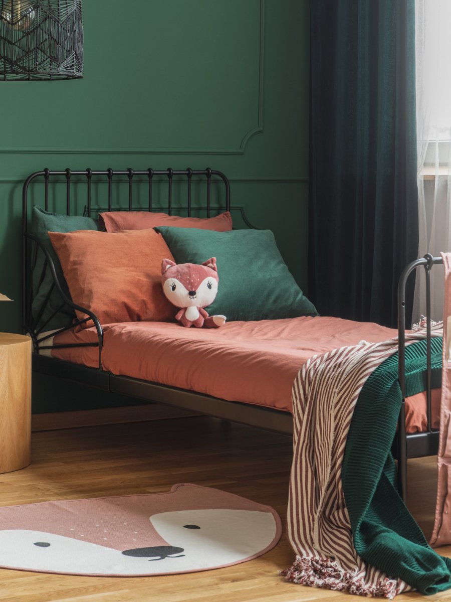 Cozy bedroom with green walls, black metal bed frame, rust and green bedding, fox plush toy, and fox-shaped rug